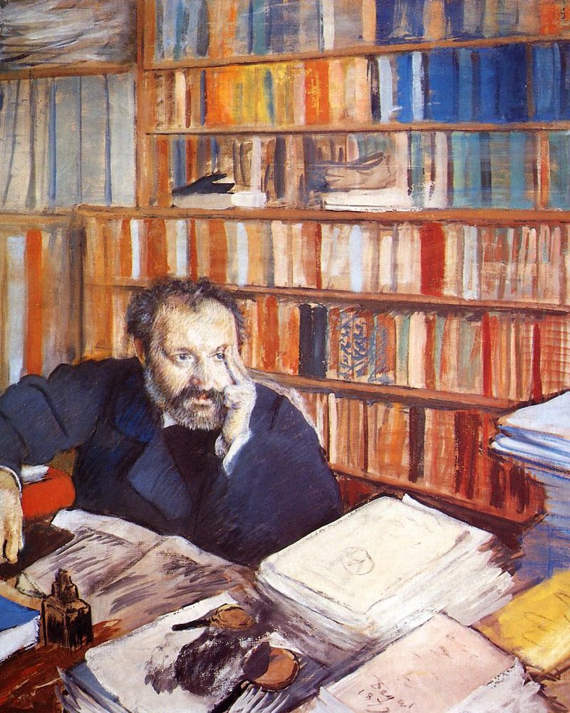 A writer at a desk piled with papers, in front of full bookshelves